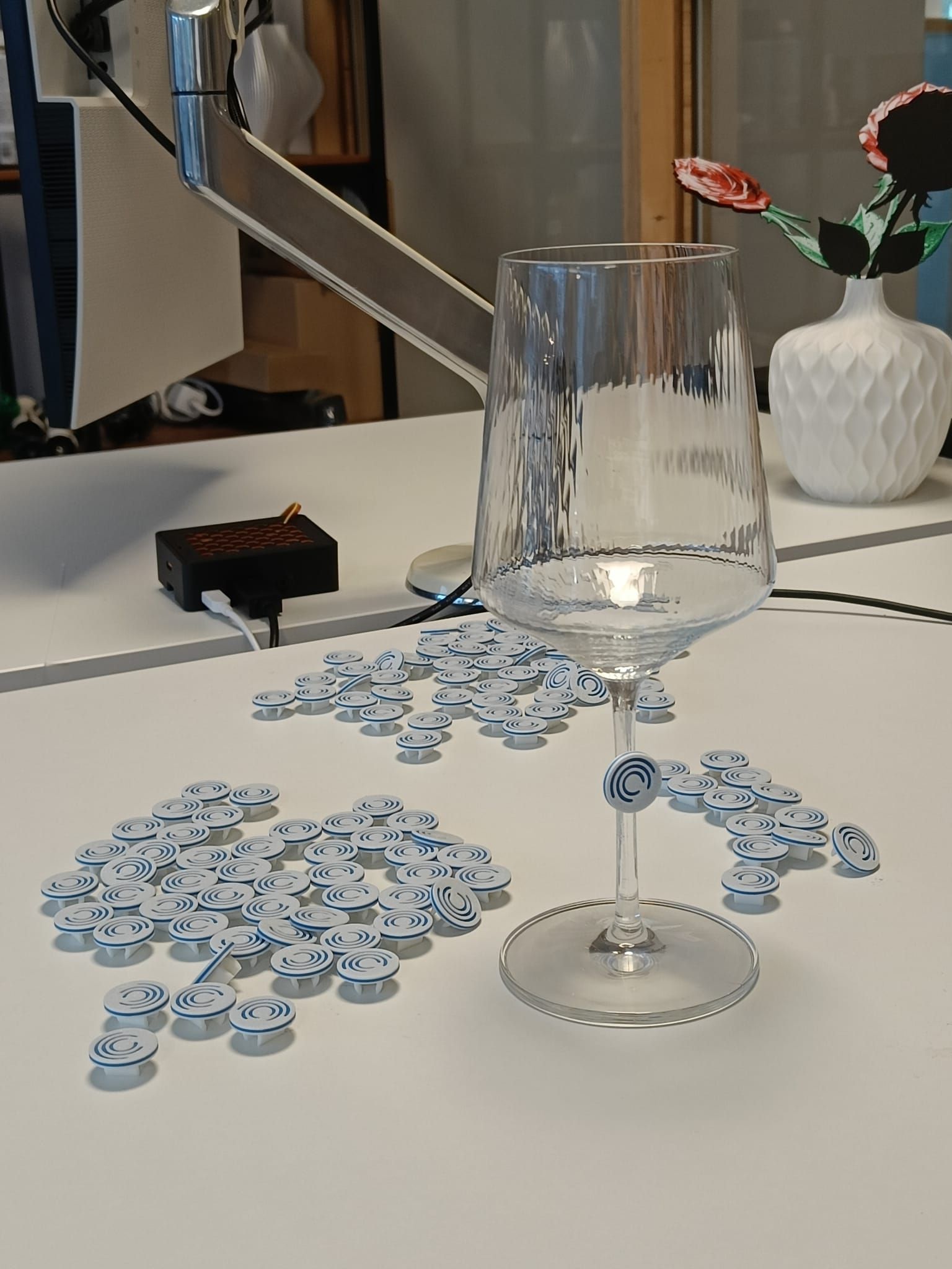 Dozens of round white and blue logo clips on a table, one clipped to the stem of a wine glass