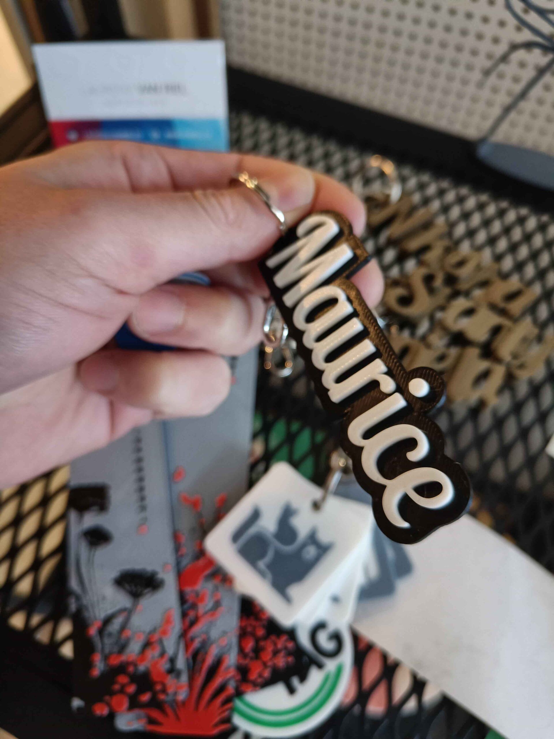 A hand holding a keychain spelling Maurice in raised white script on a black base