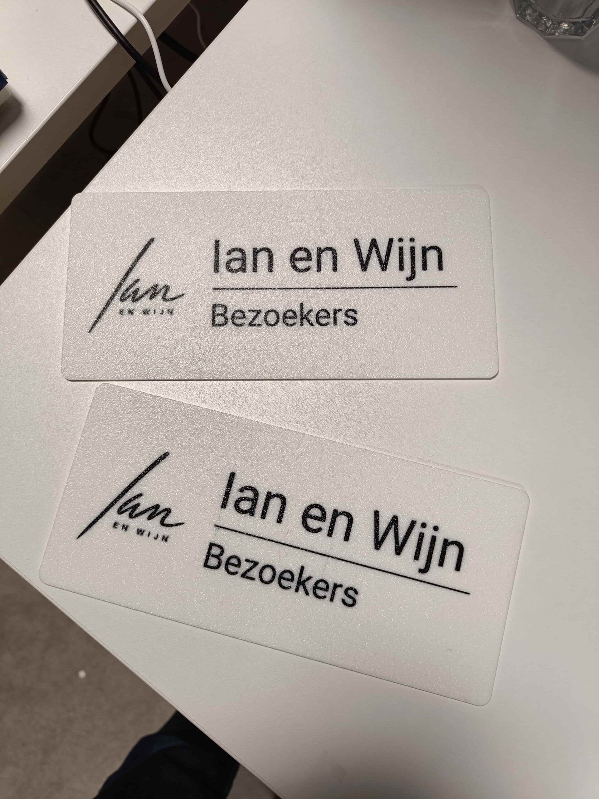 Two white printed parking signs with the Ian en Wijn logo and the word Bezoekers in black